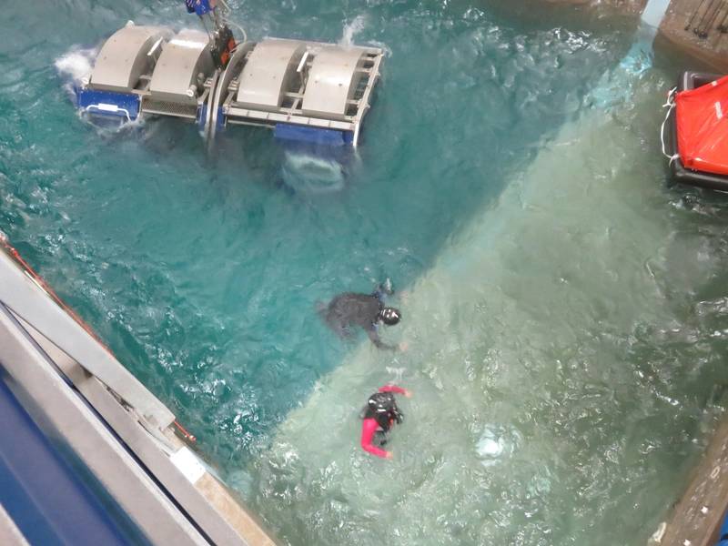 Водолаз (в черном цвете) помогает офшорному рабочему (в красном) в достижении безопасности спасательного плота справа от изображения. (Фото: Том Маллиган)