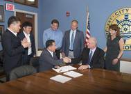 The fifth largest steel producer in the world, South Korea’s POSCO, announced it will build a wire rod processing center at the Port of Indiana-Jeffersonville. Left to right Woon Hyun Yeo, Sales Director, POSCO; Kyu Tae Kim, Finance Director, POSCO; Kenny Hwang (sitting), President, POSCO-AAPC; Rob Waiz, Economic and Re-development Director, City of Jeffersonville; Mike Moore, Mayor, City of Jeffersonville; Scott Stewart, Port Director, Port of Indiana-Jeffersonville; Wendy Dant Chesser, CEO, On