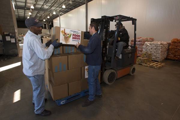 Newport News Shipbuilding employees Rudolph Johnson (left) and Wesley Dunlow (right) load boxes of donated food on to pallets at the Virginia Peninsula Foodbank. Foodbank employee Reginald Williams operates the forklift. Photo by John Whalen